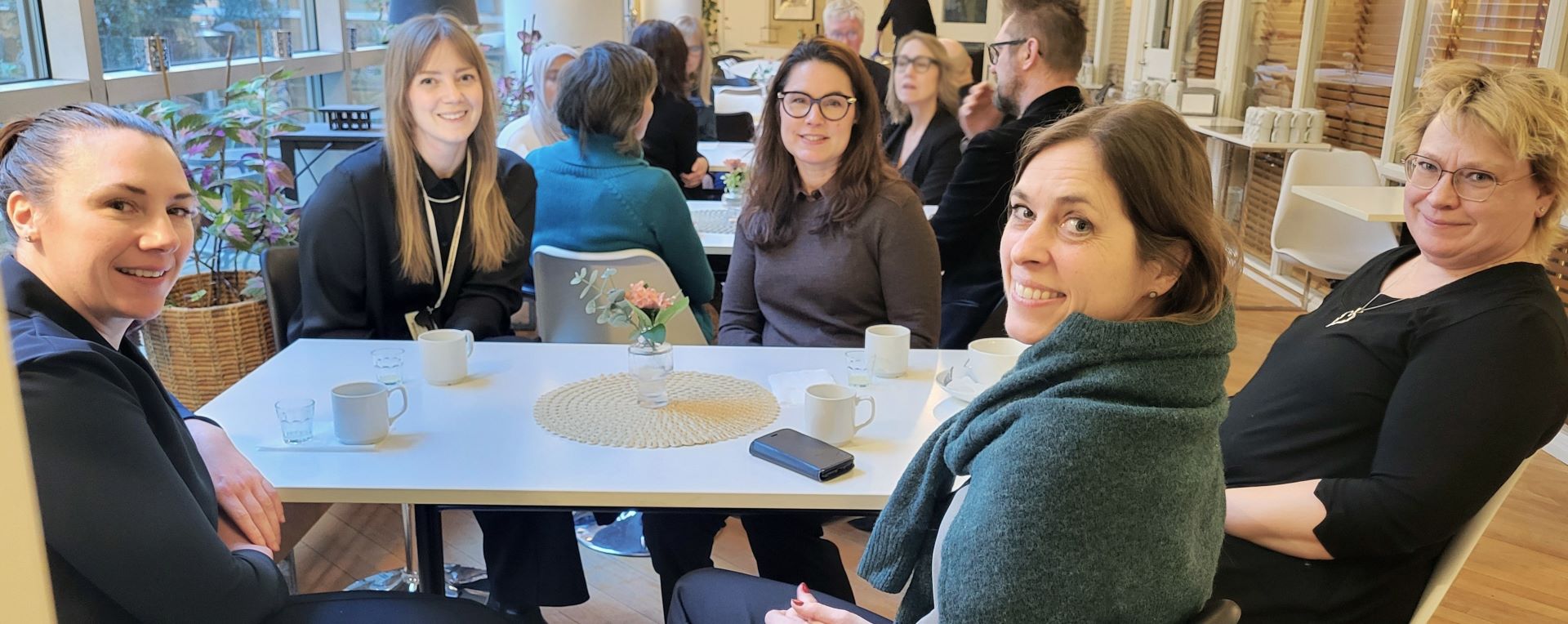 En grupp kvinnor sitter och fikar men vänder sig mot kameran.