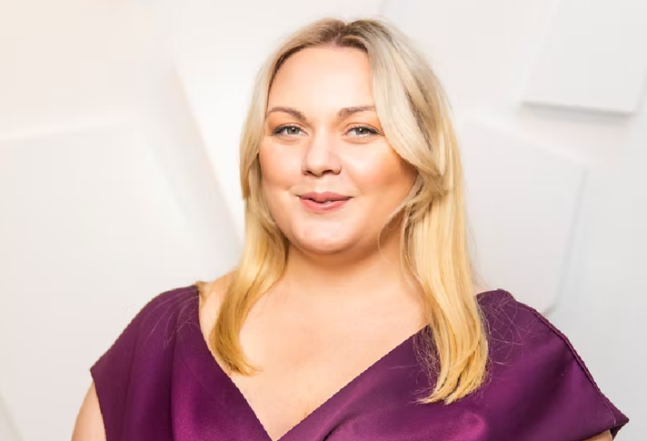 En kvinna i långt blont hår i en lila klänning.