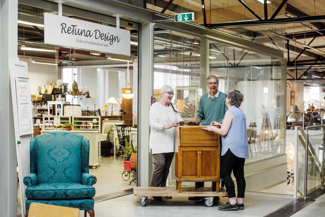 Tre personer står runt ett skåp på en vagn utanför Retuna Design.