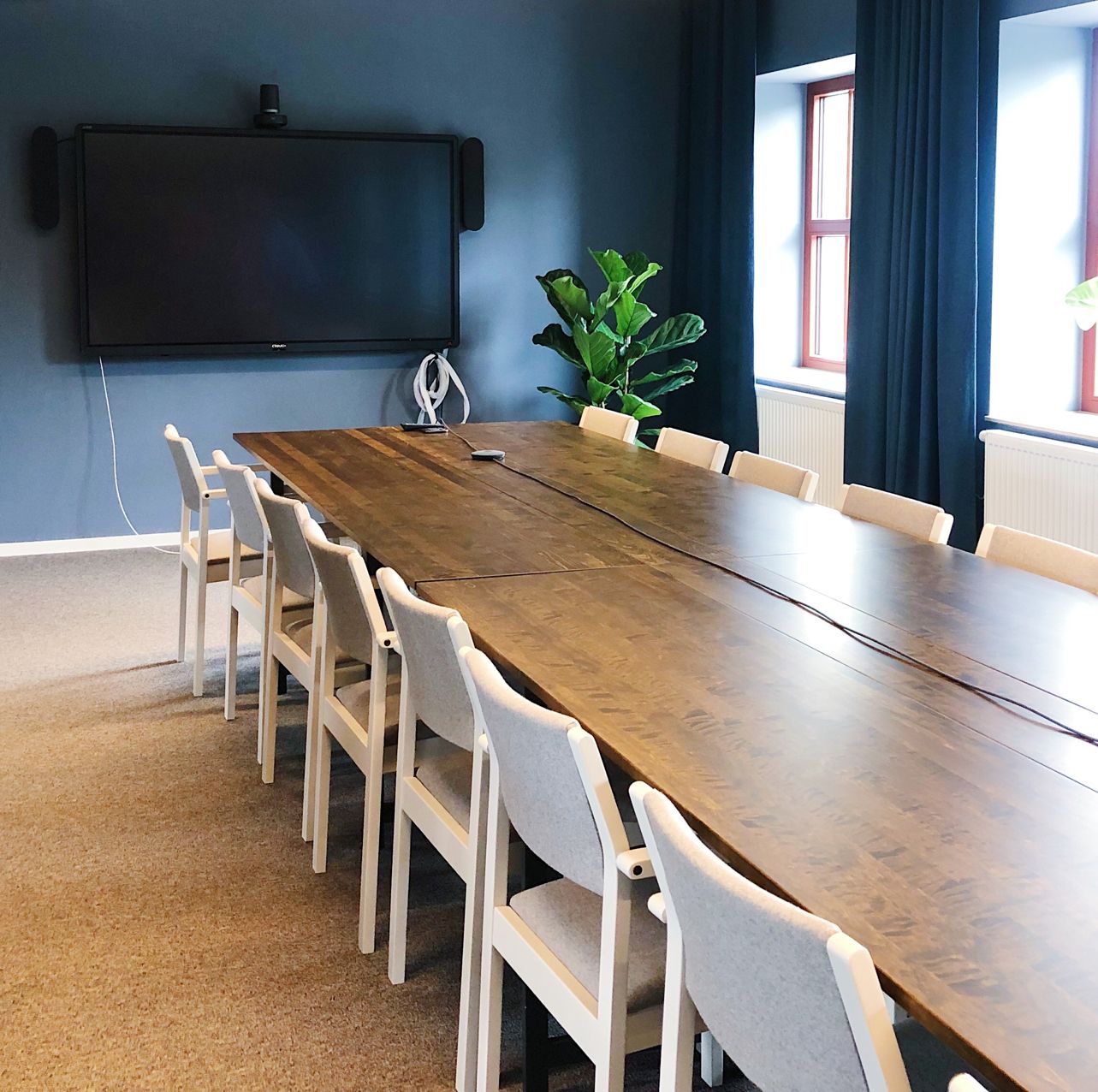 Konferensbord med renoverade stolar, rummet går i blått med blå gardiner. På väggen sitter en tv
