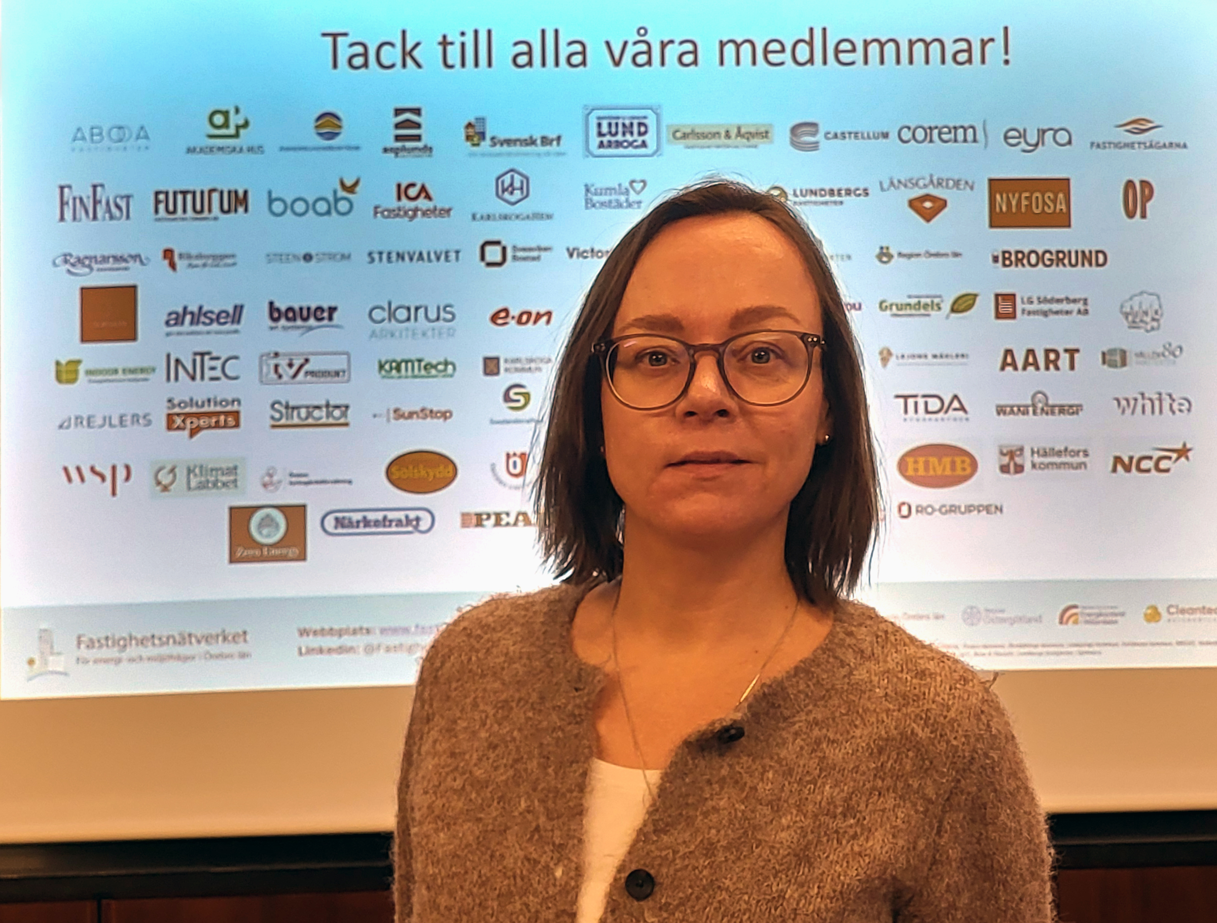 Camilla står framför en skärm med alla Fastighetsnätverkets medlemmars loggor. 