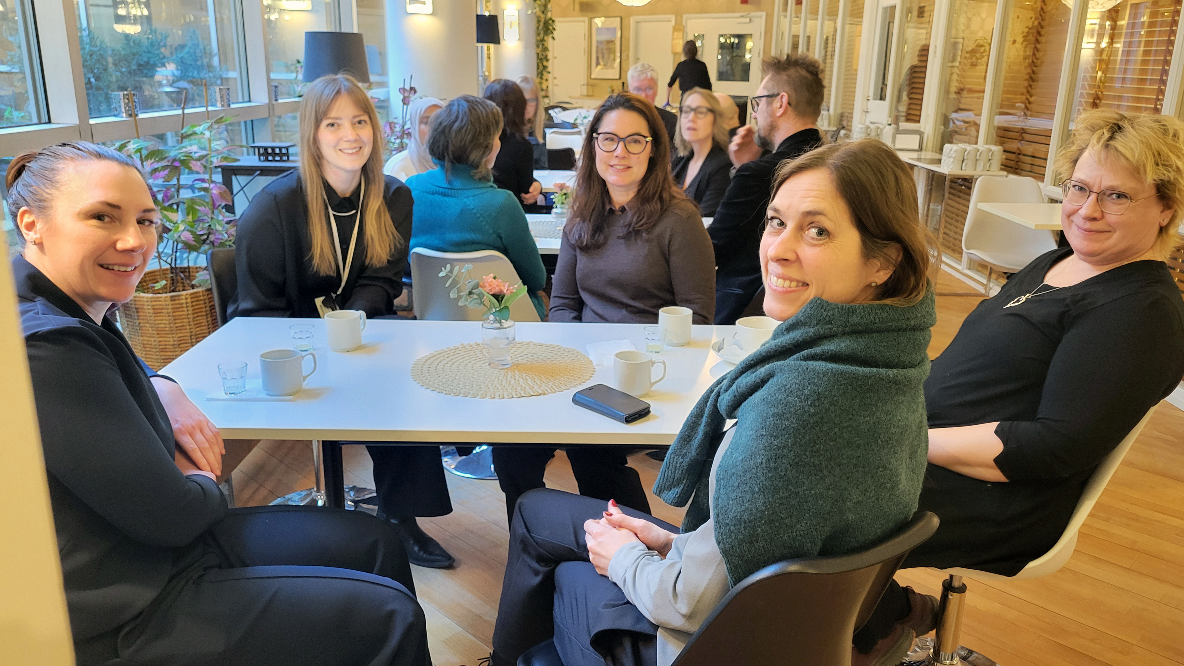 I förgrunden kvinnor som sitter vid fikabord. I bakgrunden flera fikabord.