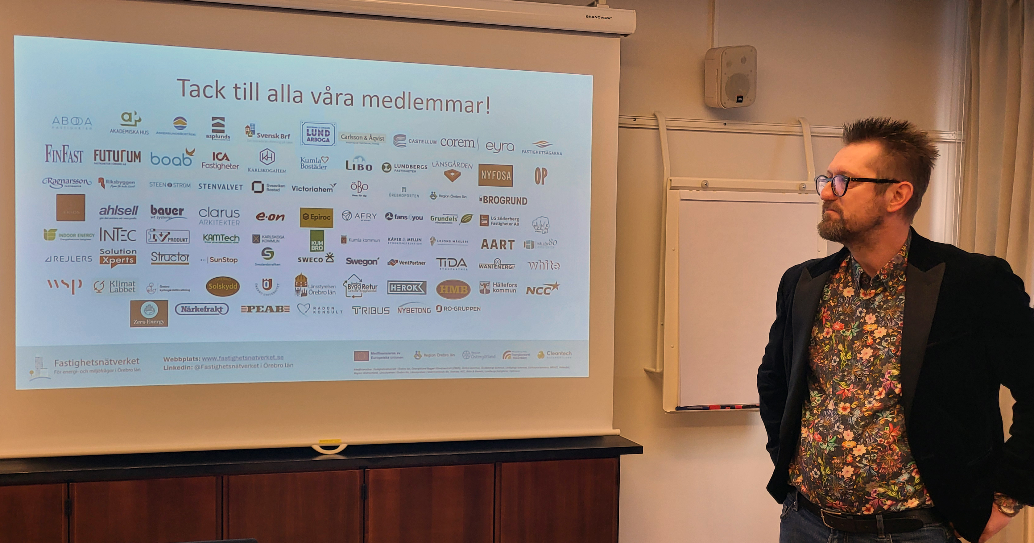 Lennart en man med brunt hår, skägg och glasögon  står och tittar på skärmen med alla medlemmars loggor