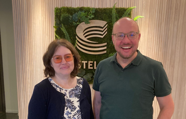 Mörkhårig kvinna i blåvit blommig känning med en mörk kofta och en man med grön pikétröja