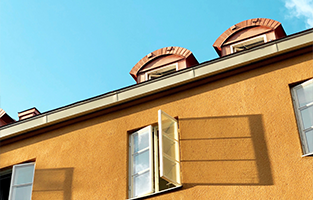 Ett gul hus i grodperspektiv med blå himmel. Huset har ett fönster öppet
