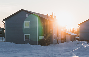 Bild på ett hus i grått med snö i motljus